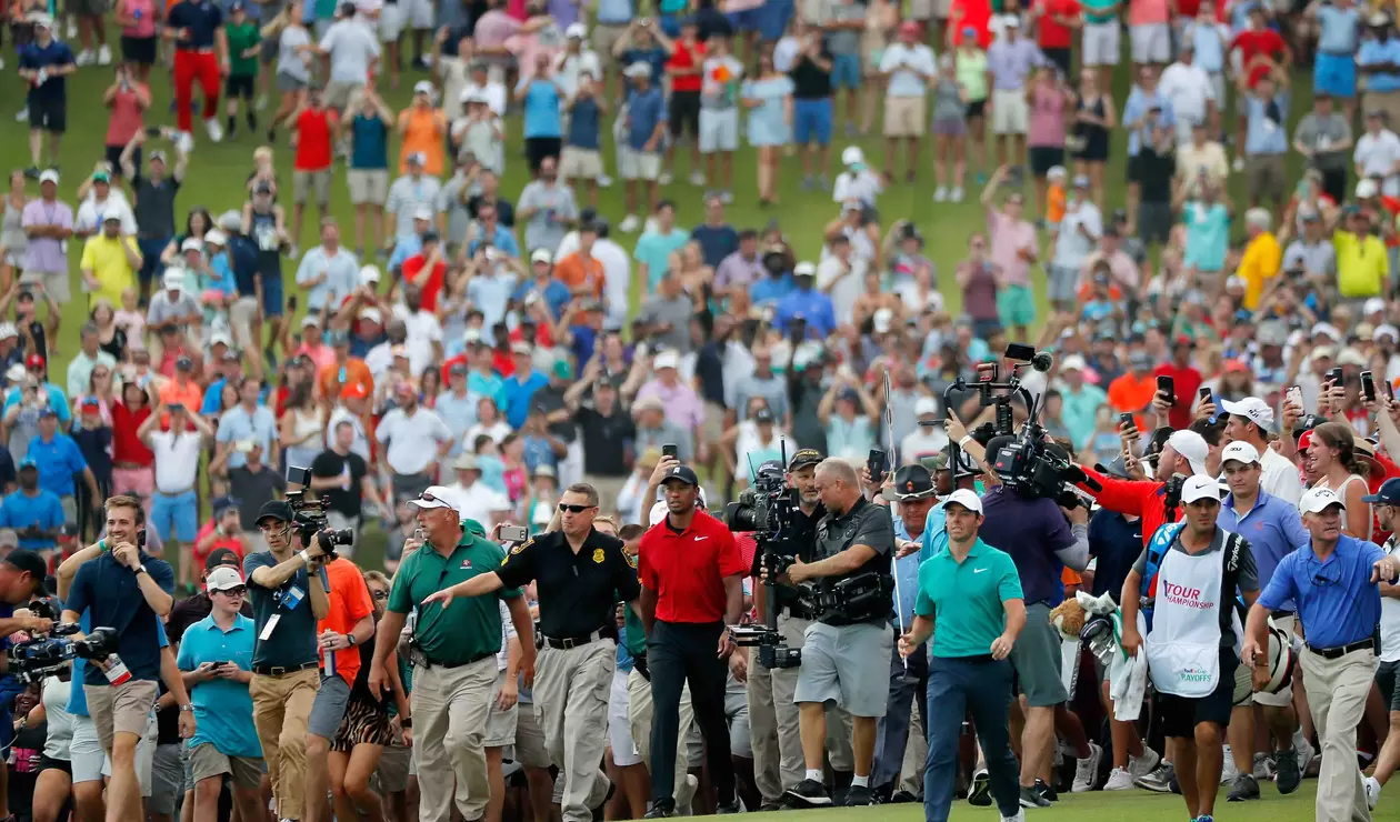 Tiger Woods y Rory Macilroy caminan con una orda de aficionados detrás suyo.